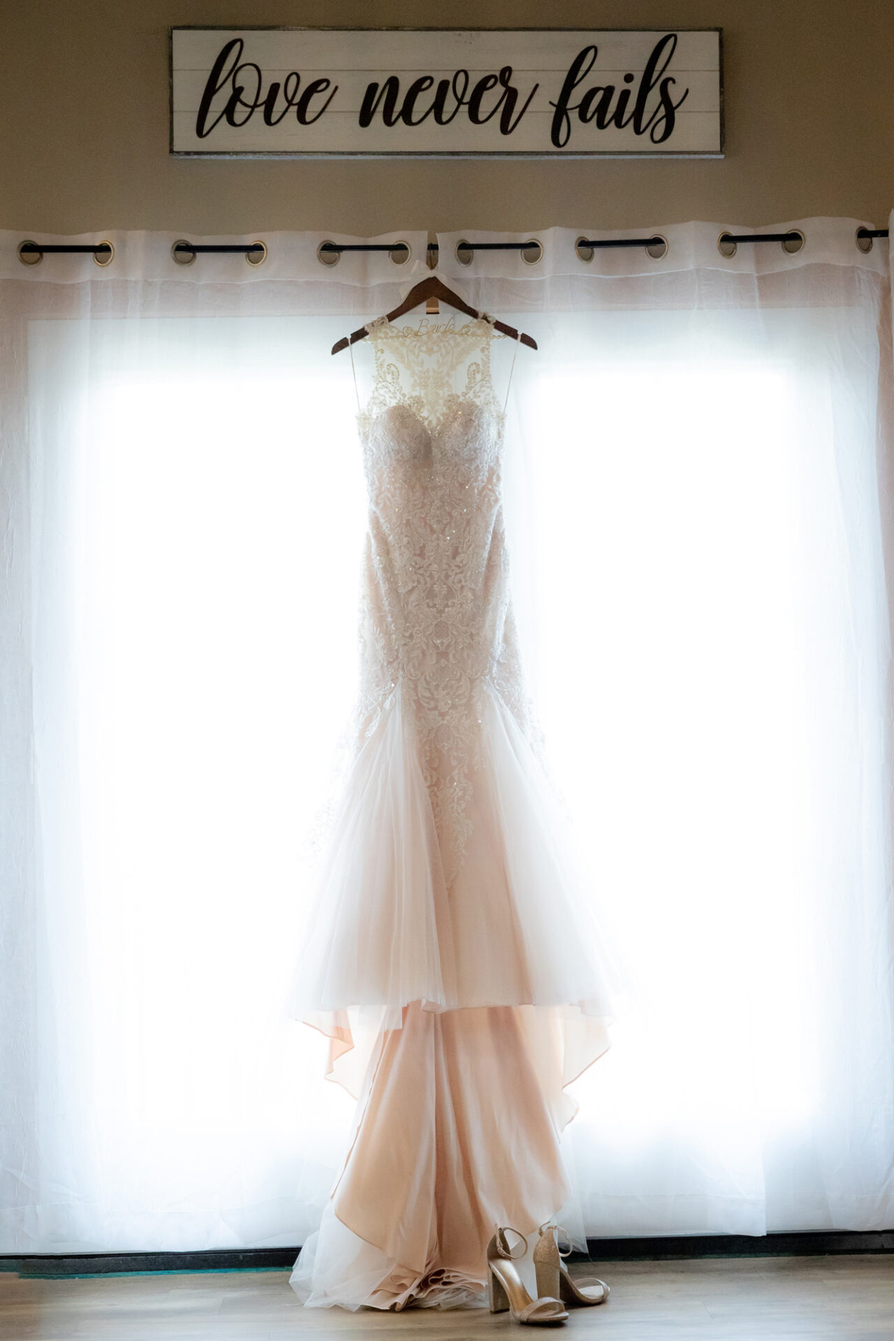 Cream-colored beaded wedding dress hung on a hanger placed against a curtain