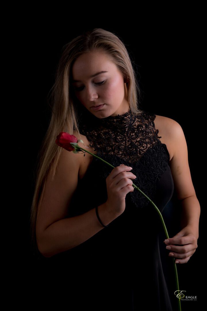 A woman in a black dress holding a long-stemmed rose